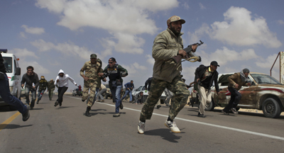 Libyan rebels and journalists run for cover as pr-Qaddafi forces shell rebel positions just outside Brega. (AP/Altaf Qadri)