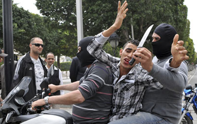 Masked plainclothes police officers take away an alleged rioter on a motorbike during clashes in Tunis. (AP/Chokri Mahjoub)