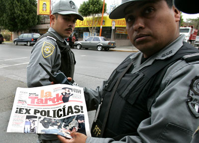 A Mexican Federal Police officer displays a newspaper with the headline 'Ex-Police!' over pictures from a recent murder in Nuevo Laredo, January 25, 2006. (AP/Gregory Bull)