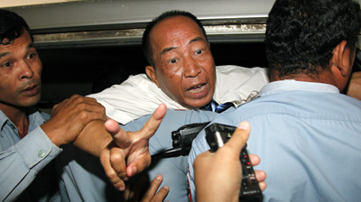 Police escort Mam Sonando into a car after a court sentenced him to 20 years. (AFP)