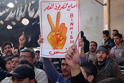 This image provided by Edlib News Network shows an anti-Syrian regime protester holding up a placard reading: 'the victory fingers over the Place (the presidential palace),' during a demonstration at Binnish village, Idlib province, on Friday. (AP/Edlib News Network ENN)