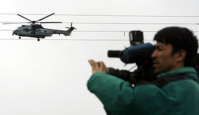 An Afghan journalist films in Kabul as a military helicopter flies above. (Reuters/Ahmad Masood)