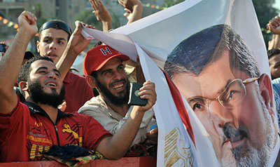 Journalists report being harassed, censored, and attacked amid clashes between supporters and opponents of ousted President Morsi. Here, Morsi supporters hold up his portrait and shout slogans. (AFP/Fayez Nureldine)