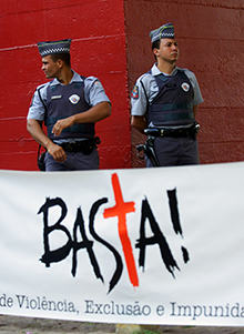 الشرطة البرازيلية تراقب متظاهرين يحتجون على جريمة قتل أحد الصحفيين عام 2002. تقول اللافتة
