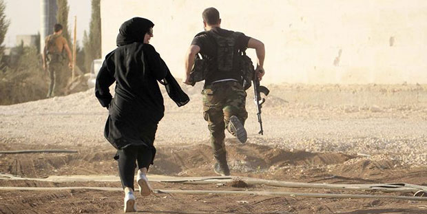 10 Ekim 2014 günü, Suriye'nin Halep şehrinde bir kadın muhabir keskin nişancıları atlatırken bir isyancı ile beraber koşuyor.  (Reuters/Jalal Al-Mamo)