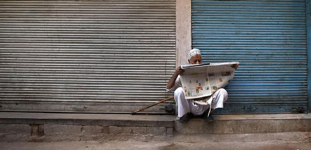 A man reads a newspaper in front of closed shops along the roadside in Delhi, India, on October 10, 2014. (Reuters/Ahmad Masood)