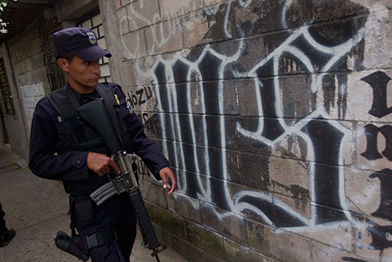 In this 2014 file photo, a policeman walks next to graffiti from the Mara Salvatrucha criminal gang. If his recent conviction on defamation charges is upheld on appeal, TV reporter Ariel Armando D'Vicente faces three years in prison and a three-year ban on practicing journalism in connection with reports alleging police took bribes from gangs involved in smuggling. (AP/Esteban Felix)