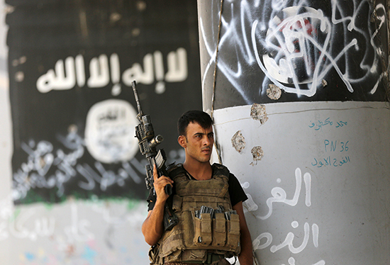 A member of Iraq's counter-terrorism forces stands guard in front of graffiti left behind by fleeing members of the Islamic State group in Fallujah, June 27, 2016. (AP/Hadi Mizban)