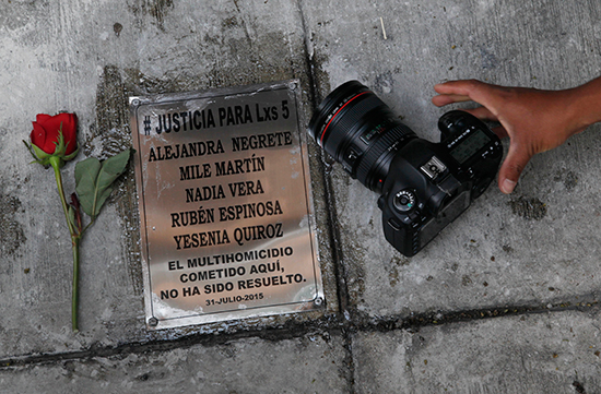 Un fotógrafo coloca su cámara junto a una placa en memoria del fotoperiodista Rubén Espinosa y cuatro mujeres asesinadas junto con él en Ciudad de México en 2015, en el aniversario de las muertes, el 31 de julio de 2016. En el momento del asesinato, Espinosa trabajaba para el semanario investigativo Proceso y para otros medios del estado de Veracruz. (AP/Marco Ugarte)