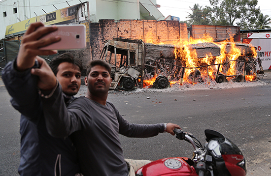 Men in Bangalore, India, take a selfie in front of a truck protesters had set ablaze, September 12, 2016. (AP/Raijaz Rahi)