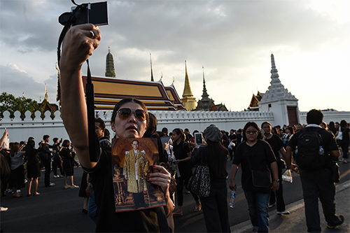 A woman takes a selfie with a picture of King Bhumibol Adulyadej after the hearse carrying his body goes by. News broadcasts have been replaced with royal footage after the king's death. (AFP/Lillian Suwanrumpha)