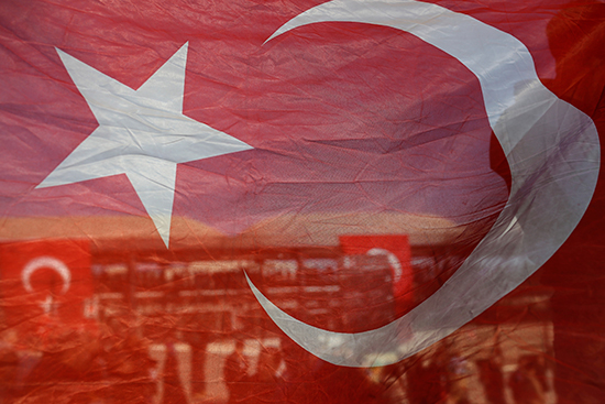 Seen through a Turkish flag, people gather outside Istanbul's Vodafone Stadium to pay respects to those killed in a bombing, December 11, 2016. Turkish authorities imposed a ban on coverage of the attack. (AP/Emrah Gurel)