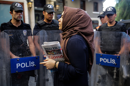 A woman holds a copy of Ozgur Gundem in front of a police barricade in August 2016. The publisher of the pro-Kurdish daily, which was ordered shut last year, has been detained. (AFP/Yasin Akgul)