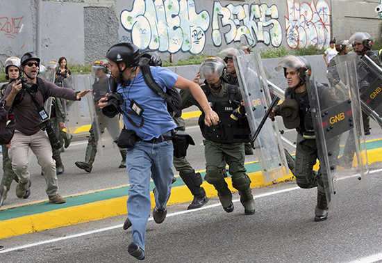 Un fotoperiodista de Reuters corre mientras efectivos de la Guardia Nacional Bolivariana avanzan durante una protesta fuera del Tribunal Supremo de Justicia en Caracas el 31 de marzo. Varios periodistas fueron heridos cubriendo los disturbios. (AP/Ariana Cubillos)