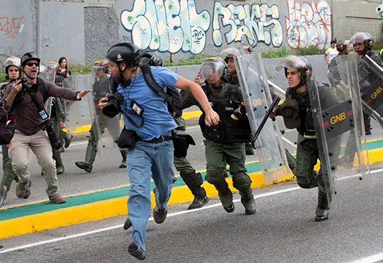 A Reuters photojournalist runs as Venezuelan National Guard soldiers charge during a protest outside the Supreme Court in Caracas on March 31. Several journalists have been injured covering the unrest. (AP/Ariana Cubillos)