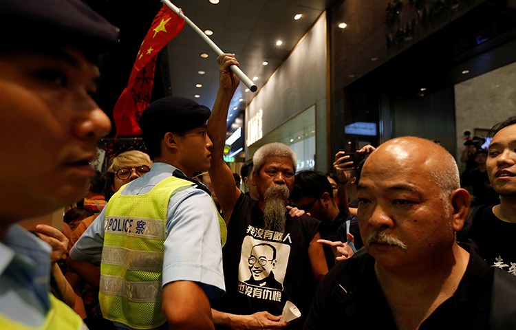 A protester carrying a defaced Chinese national flag is blocked by a police officer during a march to mourn the death of Nobel laureate Liu Xiaobo, in Hong Kong, July 15, 2017. A court in Dali, China, on August 3, 2017, sentenced journalist Lu Yuyu to four years in prison for his work documenting protests on social media. (Reuters/Bobby Yip)