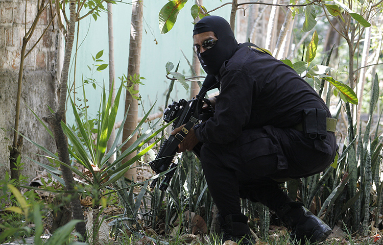 In this April 5, 2016 photo, a masked and armed policeman crouches as he patrols a gang controlled neighborhood in San Salvador, El Salvador. Journalists at two publications received threats on social media after one of the outlets published a story critical of security forces. (AP Photo/Alex Peña)