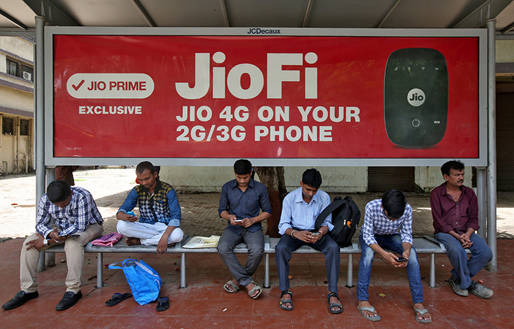 Commuters in Mumbai use their mobile phones as they wait at a bus stop with a telecom advertisement on July 10. The majority of India's internet users connect via their mobile devices. India recently adopted a rule that allows the government to temporarily shut down internet and telecommunications services in the event of an emergency. (Reuters/Shailesh Andrade)