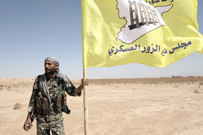 A fighter from Deir al-Zor military council which fights under the Syrian Democratic Forces holds the council's flag in the village of Abu Fas, Hasaka province, Syria September 9, 2017. Two reporters died in car bombing attacks on October 12 in Abu Fas. (Reuters/Rodi Said)