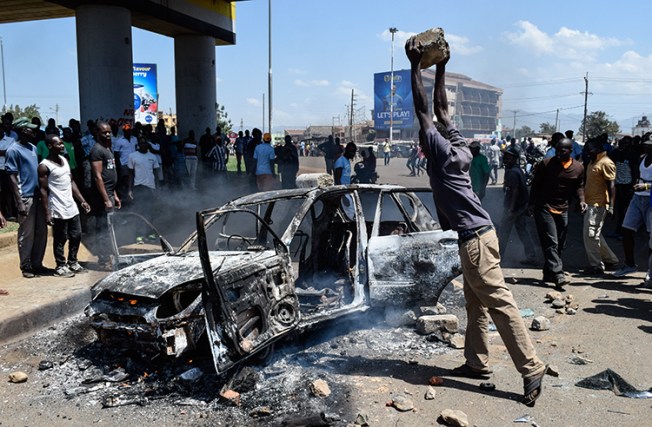 A man throws a stone on a burnt car during clashes in Kisumu on November 20 over Kenya's Supreme Court ruling on the country's election. (AFP/Brian Ongoro)