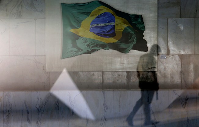 A presidential guard walks past a window that allows a view into the Planalto presidential palace's main lounge, decorated with an image of a Brazilian national flag, in Brasilia, Brazil, Thursday, April 13, 2017. (AP/Eraldo Peres)
