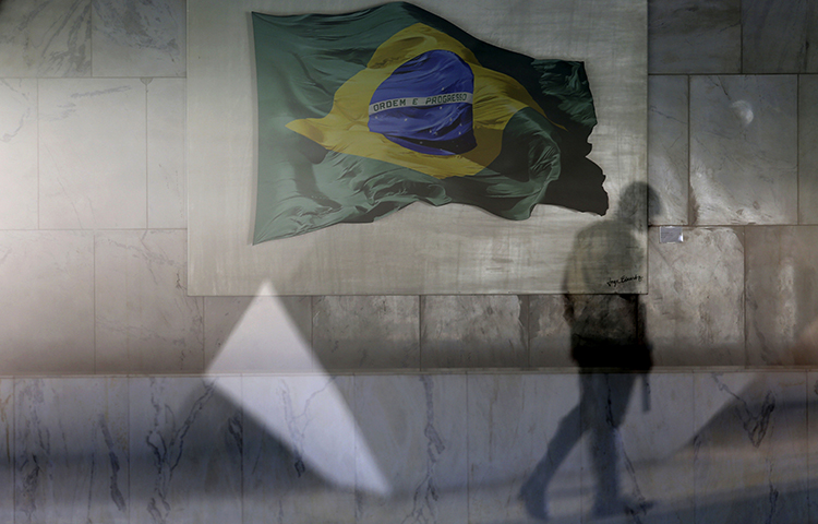 A presidential guard walks past a window that allows a view into the Planalto presidential palace's main lounge, decorated with an image of a Brazilian national flag, in Brasilia, Brazil, Thursday, April 13, 2017. (AP/Eraldo Peres)