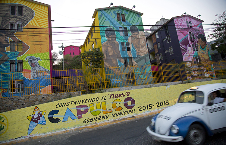 A taxi drives past the Cuauhtemoc Housing Unit and a municipal sign with a message that reads in Spanish "Building the new Acapulco" in Acapulco, Mexico on May 11, 2016. Antonio Julián Chepe said he was driving his vehicle on the highway between his hometown in Marquelia and Acapulco in Mexico's southern Guerrero state when at least six men carrying automatic rifles attacked him. (AP/ Enric Marti)