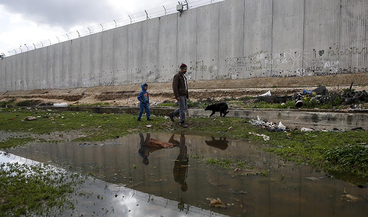 A Palestinian and a boy walk a dog along the Israeli barrier in the West Bank town of Qalqilyah in February. Israeli security forces arrested a Quds News Network reporter at his West Bank home on February 15. (AFP/Jaafar Ashtiyeh)