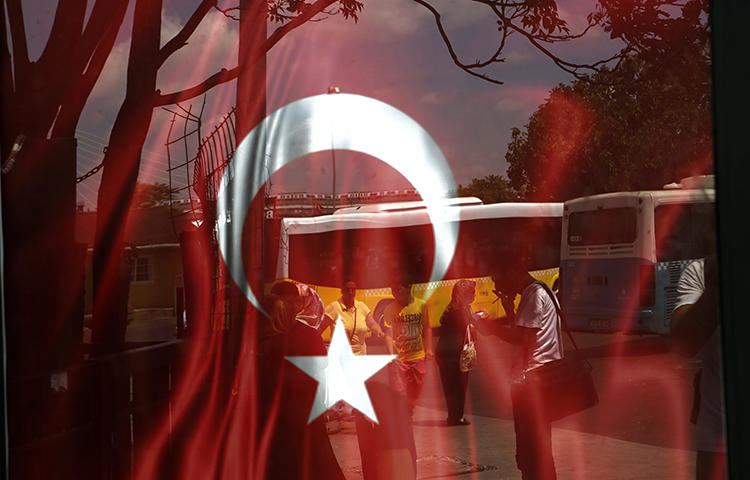 People reflected on glass with Turkish a flag at a bus station in Istanbul in July 2016. A proposed bill presented to Turkey's parliament on February 2 would force online broadcasters, including YouTube and Netflix Turkey, to be licensed and regulated by the federal TV and radio watchdog group RTÜK, according to local reports. (AP/Petros Karadjias)