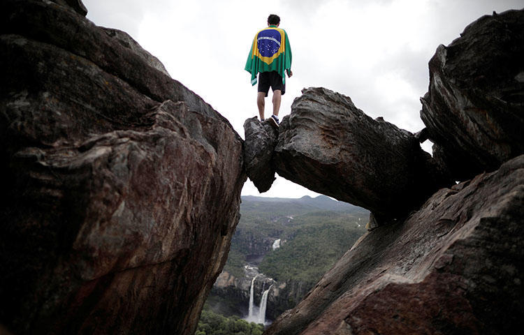 A park visitor wrapped in a Brazilian flag stands above a natural rock window in Chapada dos Veadeiros National Park in Alto Paraiso, Brazil in March 2018. At least one unidentified gunman on March 25 fired at the offices of the weekly Jornal dos Bairros, according to reports. (Reuters/Ueslei Marcelino)