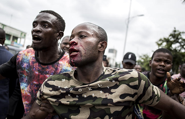 An injured man is pulled to safety after police fired warning shots to disperse a crowd at the end of a service to commemorate the victims of a crackdown on a march in Kinshasa in December 2018. (AFP/John Wessels)