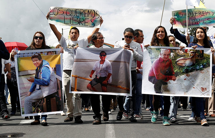 Familiares y amigos en Quito muestran fotos el 1 de abril del reportero gráfico ecuatoriano Paúl Rivas, a la izquierda, el periodista Javier Ortega, centro, y su chófer Efraín Segarra, quienes fueron secuestrados cerca de la frontera con Colombia y luego asesinados. (Reuters / Daniel Tapia)