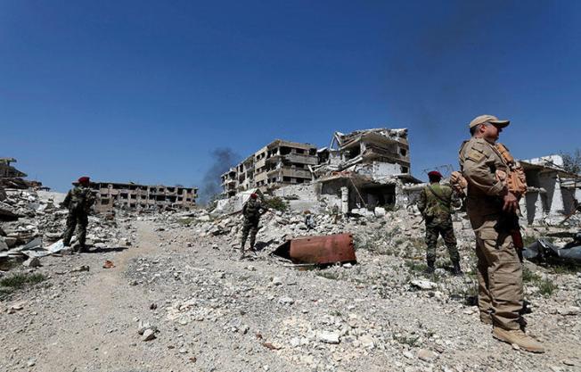 Members Syrian President Bashar Assad's forces stand guard near destroyed buildings in eastern Ghouta on April 2, 2018. Two members of a Turkish-funded militant group on March 21, 2018, attacked a Syrian cameraperson as he was covering the arrival of refugee convoys from eastern Ghouta, according to reports. (Reuters/Omar Sanadiki)