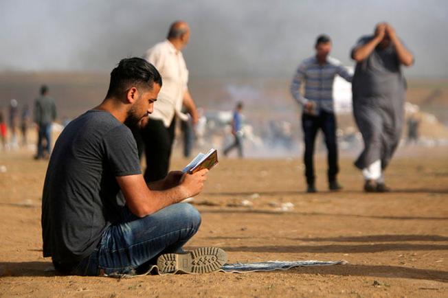 A Palestinian man reads a book during clashes with Israeli forces along the border with the Gaza strip east of Jabalia on May 18, 2018. An Israeli police officer assaulted a Palestinian journalist covering pro-Gaza protests in Haifa on May 18. (Mohammed Abed/AFP)