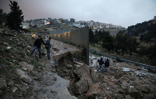 Palestinians stand next to a collapsed part of the Israeli barrier near a refugee camp in East Jerusalem on April 26, 2018. Israeli internal security forces and police on April 18 posted a Defense Ministry order to the door of Elia Youth Media Foundation ordering its closure, according to media reports. (Reuters/Ammar Awad)