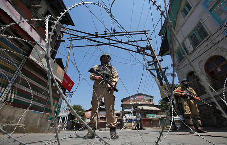 Indian policemen stand guard behind concertina wire during a strike in the town of Srinagar in the state of Jammu and Kashmir on May 21, 2018. A Kashmiri freelance photographer, Masrat Zahra, told CPJ that she has faced online harassment and threats after a photograph of her, captioned with the word
