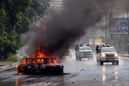 Nicaraguan police officers travel past a burning car in Managua, the site of clashes between officers and anti-government protesters. In April, CPJ's Emergencies Response Team published a safety advisory for journalists covering the protests. (Reuters/Oswaldo Rivas)