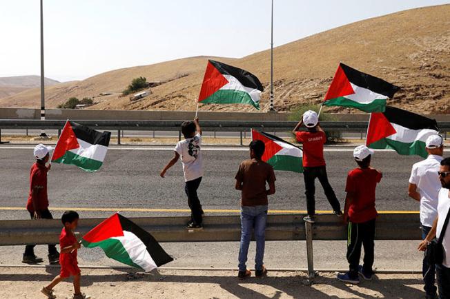 Children wave Palestinian flags on a main road leading from Jerusalem to the Dead sea at the al-Khan al-Ahmar near Jericho in the occupied West Bank on July 4, 2018. Palestinian Preventative Security Forces on July 22 detained Palestinian journalist Huthifa Abu Jamous, according to reports. (Reuters/Ronen Zvulun)