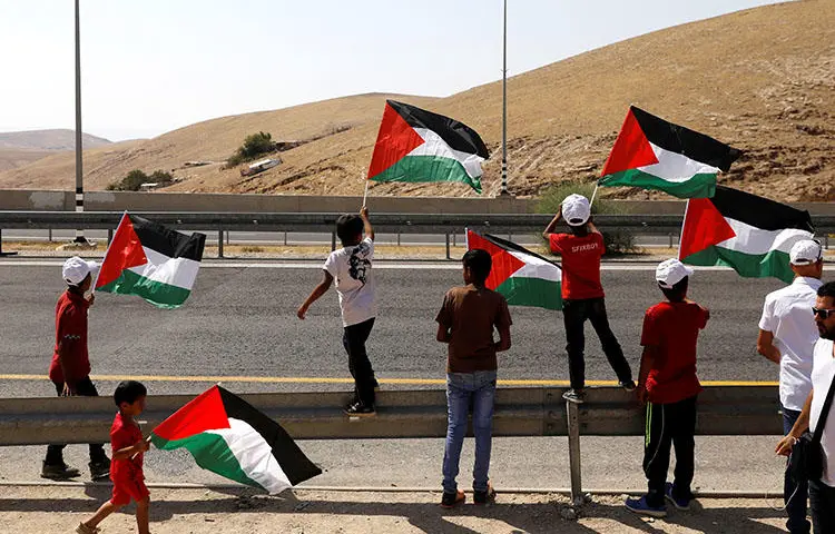 Children wave Palestinian flags on a main road leading from Jerusalem to the Dead sea at the al-Khan al-Ahmar near Jericho in the occupied West Bank on July 4, 2018. Palestinian Preventative Security Forces on July 22 detained Palestinian journalist Huthifa Abu Jamous, according to reports. (Reuters/Ronen Zvulun)