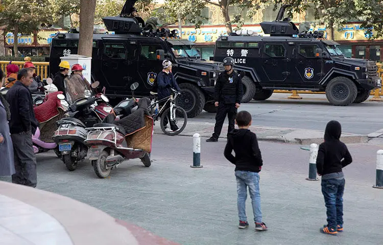 Residents watch a convoy of security personnel and armored vehicles in a show of force through central Kashgar in western China's Xinjiang region in November 2017. China declined to renew the visa of a BuzzFeed journalist who reported on alleged human rights violations in the region. (AP/Ng Han Guan)