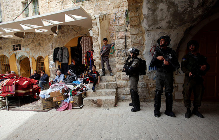 Israeli forces stand guard as Palestinians sit outside shops in Hebron, in the West Bank on April 3, 2018. At least seven Palestinian journalists have been arrested since July 31, according to news report. (Reuters/Mussa Qawasma)