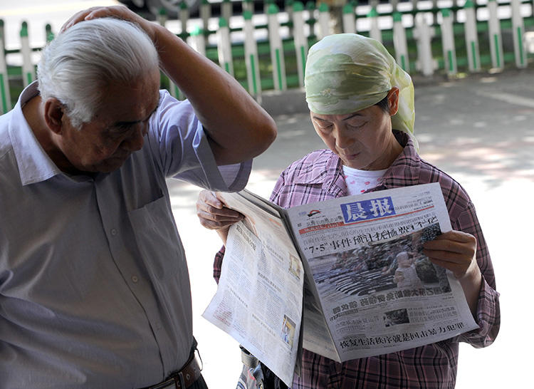 A Chinese Muslim woman reads a newspaper along a street in Urumqi, in China's Xinjiang region, on July 9, 2009. China arrested a Uighur editor and newspaper directors for being 'two-faced' in July and August 2018. (AFP Photo/Goh Chai Hin)