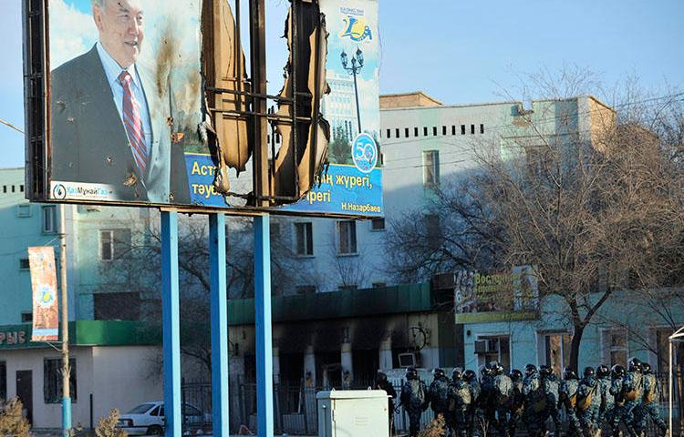 Kazakh Interior Ministry troops patrol beneath a poster of President Nursultan Nazarbayev and partially burnt buildings in Zhanaozen, in December 2011, that were damaged in riots. Kazakh police detained a French journalists today while he interviewed witnesses to the 2011 violence. (Reuters/Vladimir Tretyakov)