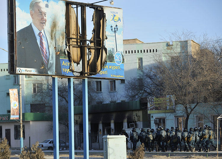 Kazakh Interior Ministry troops patrol beneath a poster of President Nursultan Nazarbayev and partially burnt buildings in Zhanaozen, in December 2011, that were damaged in riots. Kazakh police detained a French journalists today while he interviewed witnesses to the 2011 violence. (Reuters/Vladimir Tretyakov)