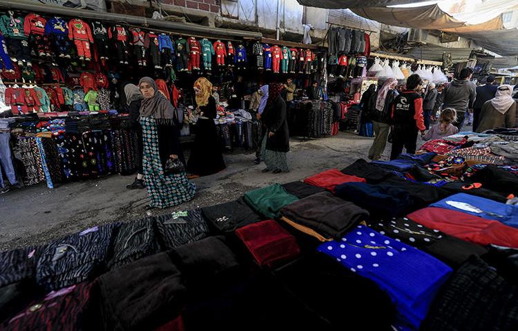 Shoppers walk on a market street in the northeastern Syrian town of Qamishli on May 2, 2018. A prominent Syrian writer was arrested and held for five days in the town in late September and early October 2018. (AFP/Delil Souleiman)