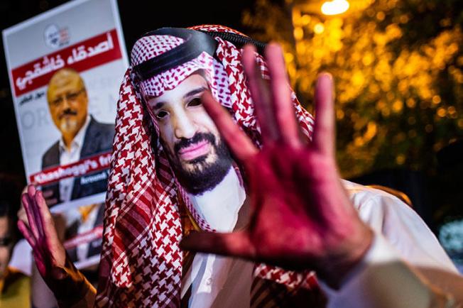 A protester wears a mask depicting Saudi Crown Prince Mohammed Bin Salman with painted hands next to people holding posters of Saudi journalist Jamal Khashoggi during the demonstration outside the Saudi Arabian consulate in Istanbul on October 25, 2018. (AFP/Yasin Akgul)