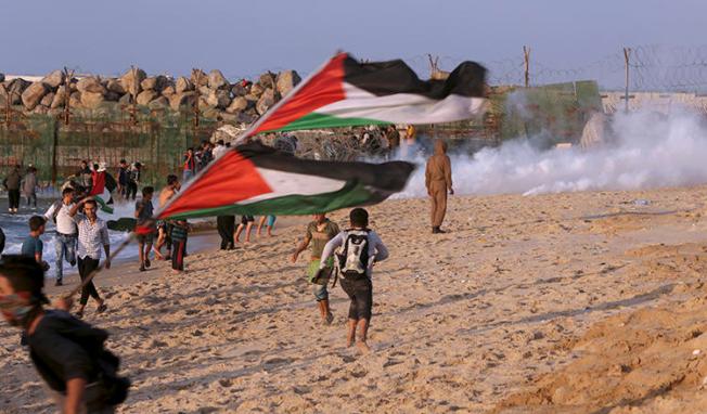 Protesters take cover from teargas fired by Israeli troops near the fence of the Gaza Strip border with Israel during a protest on the beach near Beit Lahiya, northern Gaza Strip, on November 19, 2018. (AP Photo/Adel Hana)