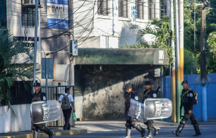 Policiais do choque caminham em frente à estação noticiosa a cabo e internet 100% Noticias, em Manágua, em 22 de dezembro de 2018, um dia depois de a emissora ter sido invadida e fechada pela polícia nicaraguense. Dois jornalistas foram presos durante a incursão. (AFP / Maynor Valenzuela)