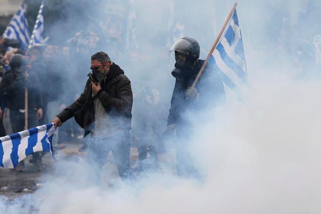 Demonstrators hold Greek flags in a cloud of tear gas during clashes at a rally in Athens on January 20, 2019. Several journalists were assaulted while covering the demonstration. (Thanassis Stavrakis/AP)