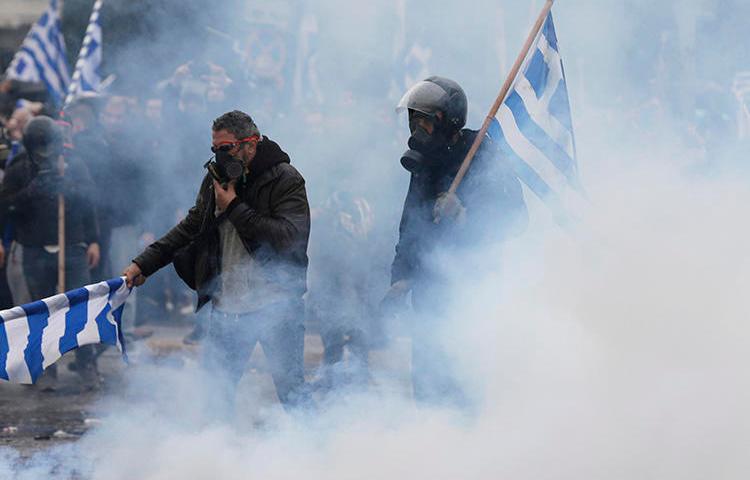 Demonstrators hold Greek flags in a cloud of tear gas during clashes at a rally in Athens on January 20, 2019. Several journalists were assaulted while covering the demonstration. (Thanassis Stavrakis/AP)